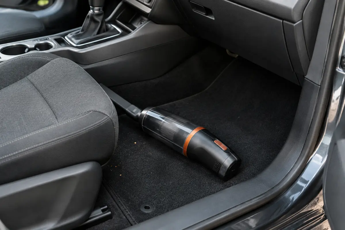 Aspirateur à main compact posé sur un tapis de voiture près de miettes à nettoyer