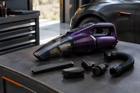 Aspirateur à main violet foncé accompagné de ses accessoires sur un tapis de voiture anthracite