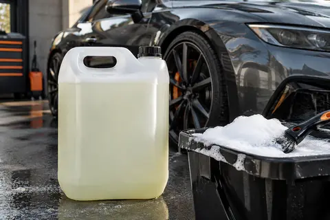 Bidon générique de shampoing mousse auto posé près d’une carrosserie anthracite dans un atelier
