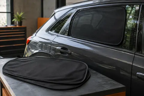 Deux pare-soleils noirs en maille extensible couvrant les vitres latérales arrière d’une voiture anthracite.