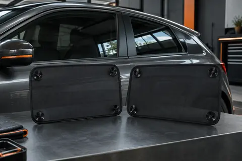 Deux pare-soleils latéraux noirs en maille nylon fixés sur la vitre d’une voiture anthracite.