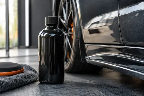 Flacon de polish liquide posé près d’une carrosserie anthracite brillante dans un atelier soigné.